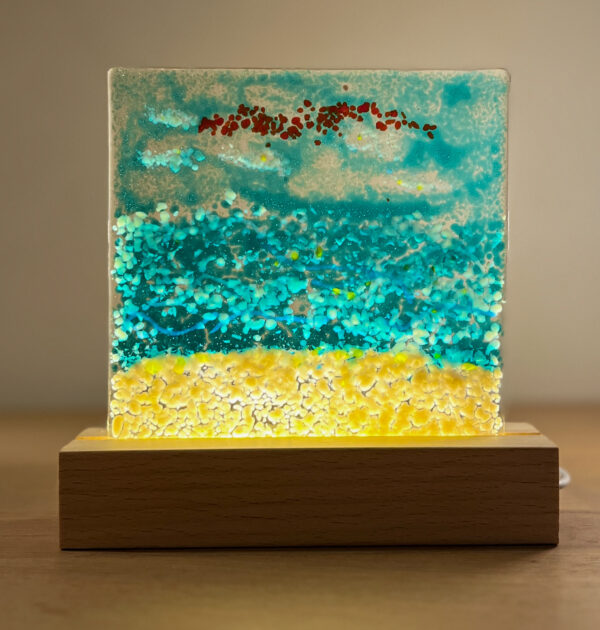 Een glascreatie - handgemaakt - op een verlichte sokkel in de reeks Strand & Zee